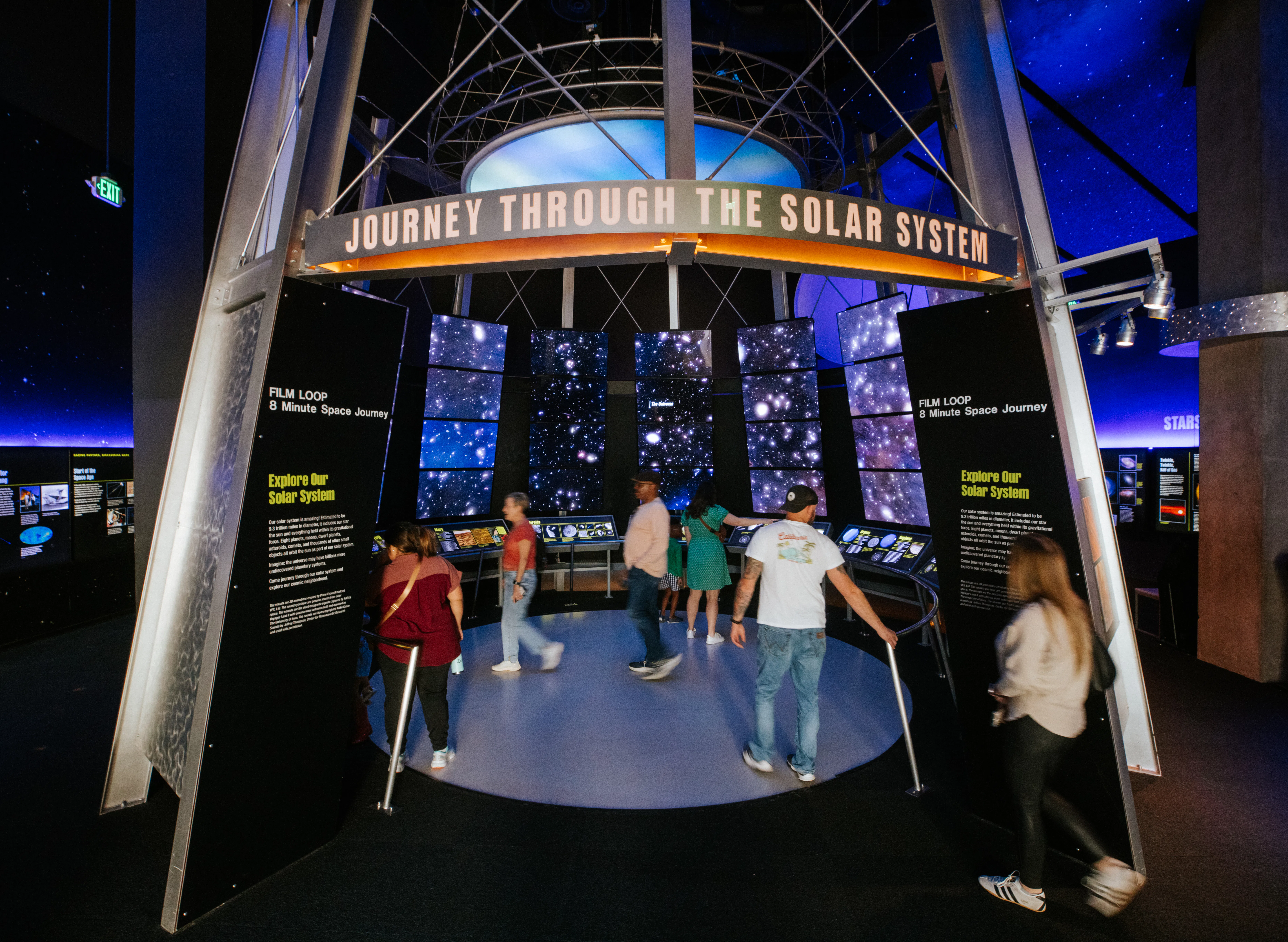 Group of people standing inside circular space surrounded by screens with space images