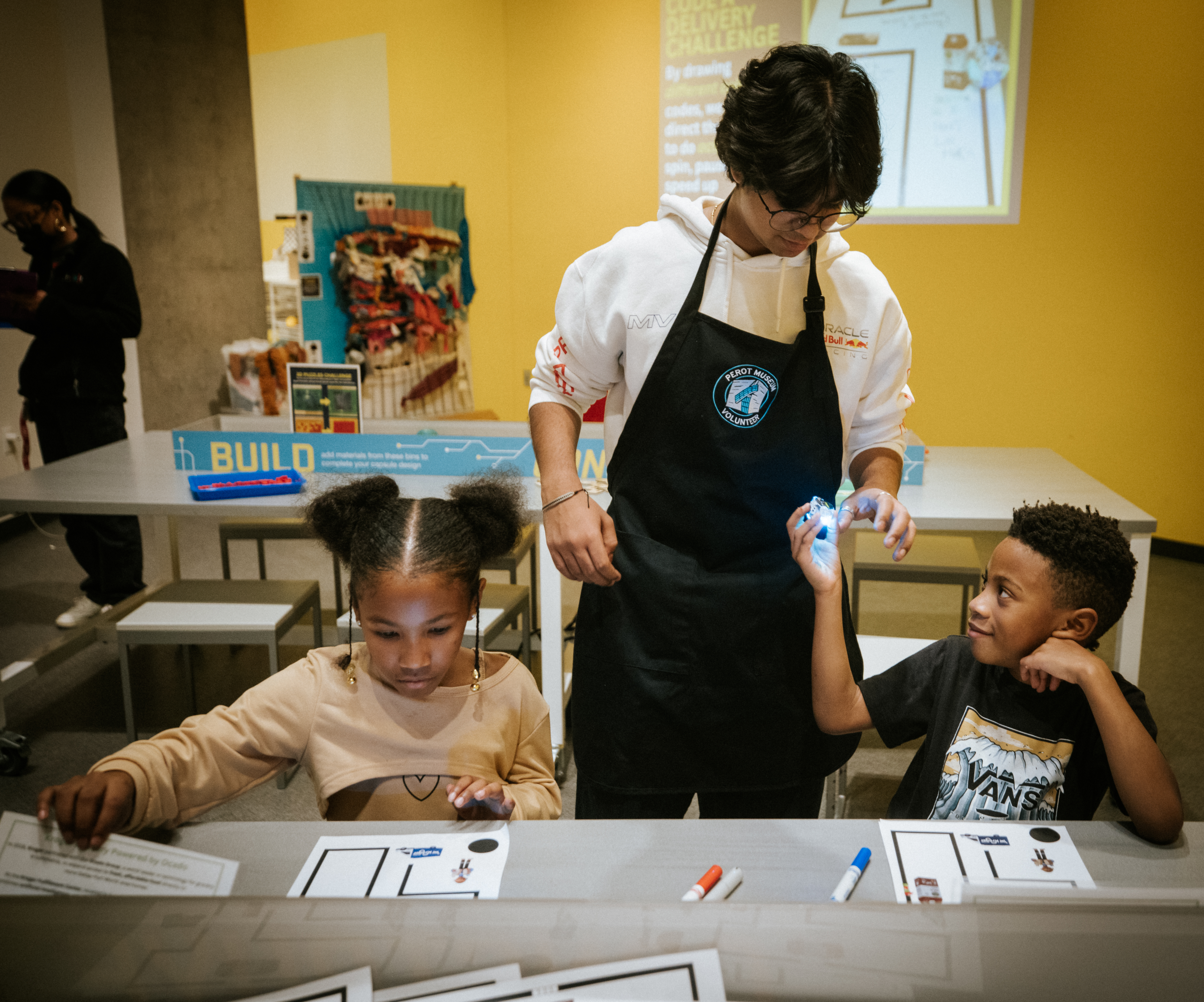 Teenage boy helping young girl and boy sitting at table doing activity