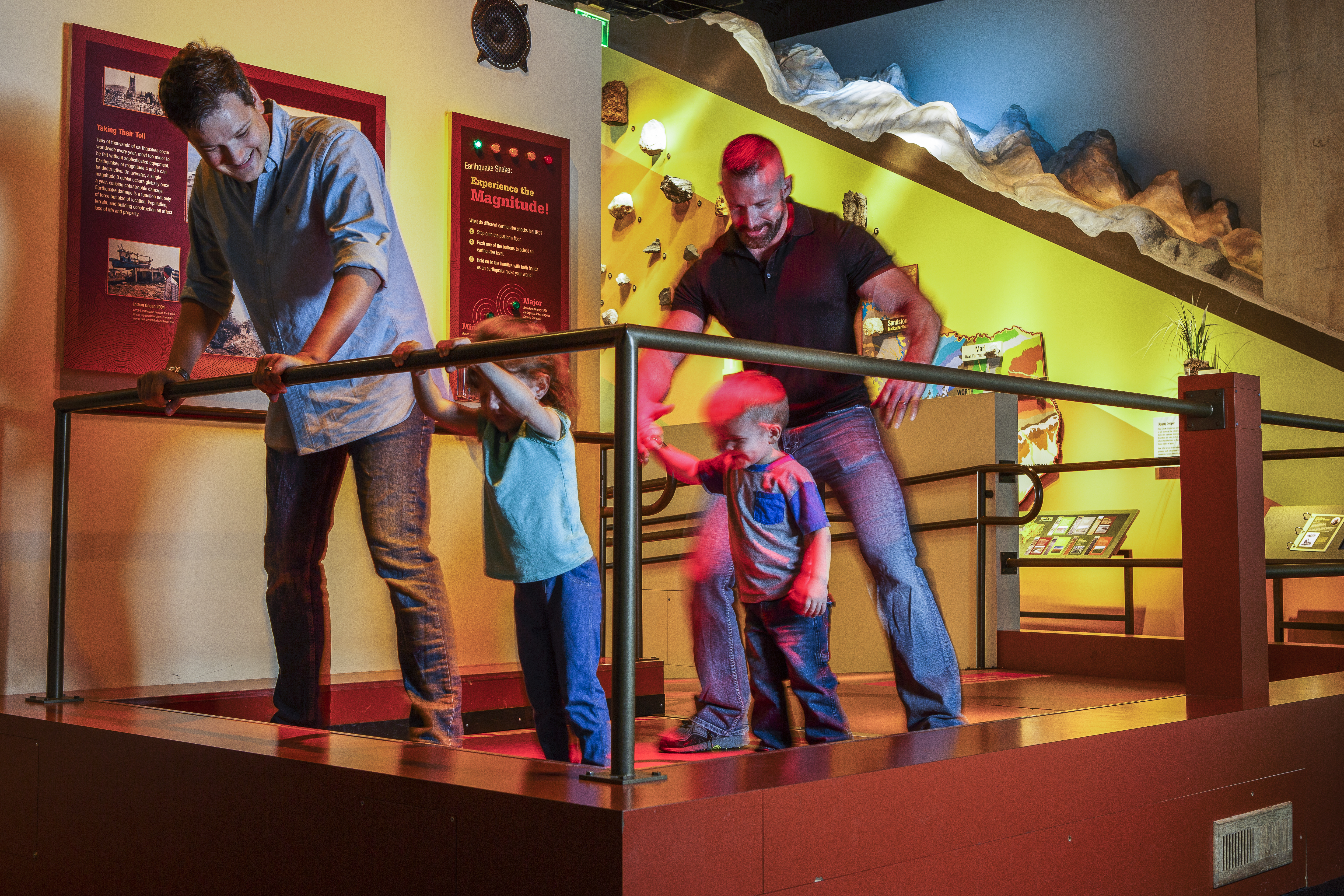 Two dads and their sons stand on the Earthquake display.