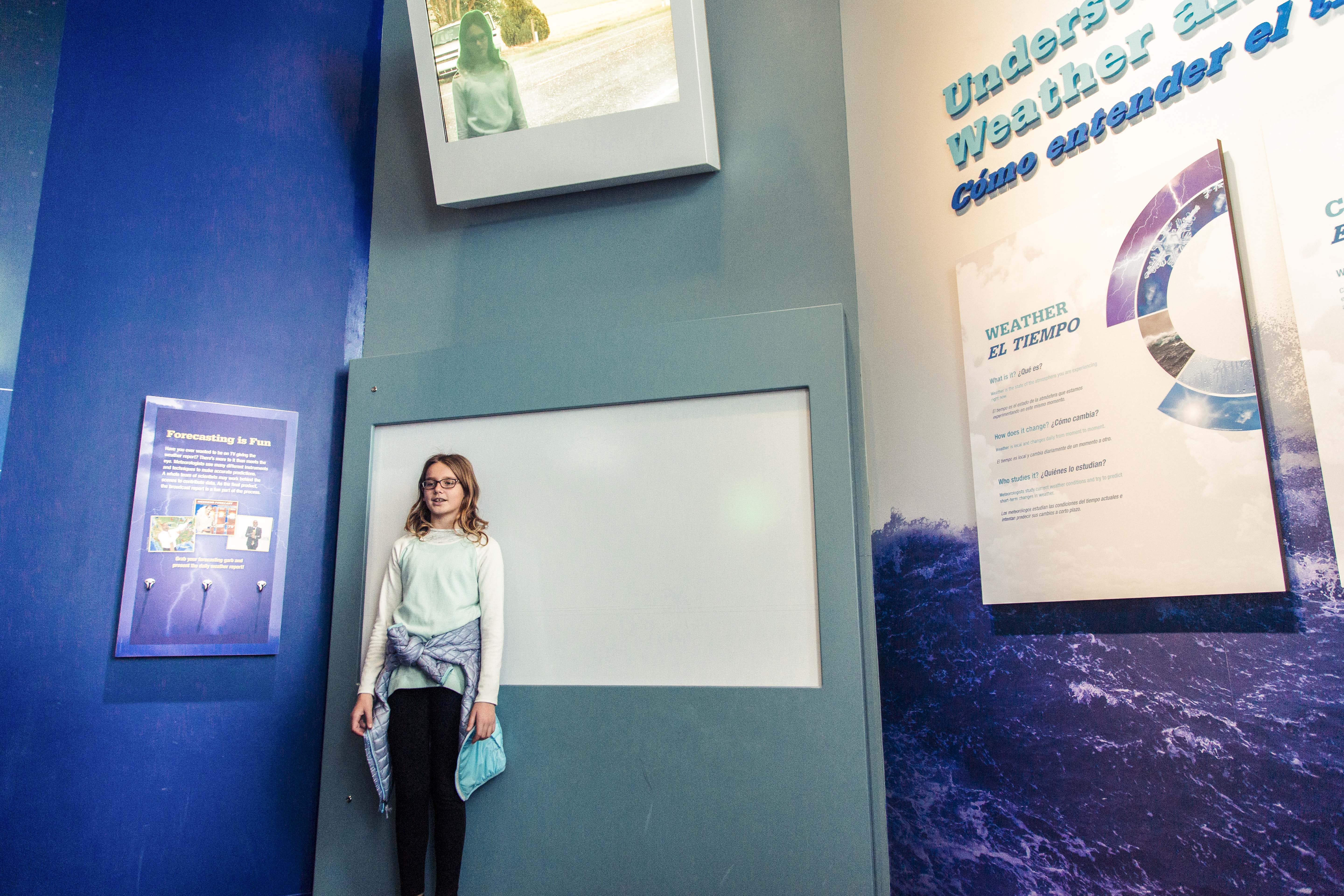 Young girl pretends to be a meteorologist in front of a green screen.