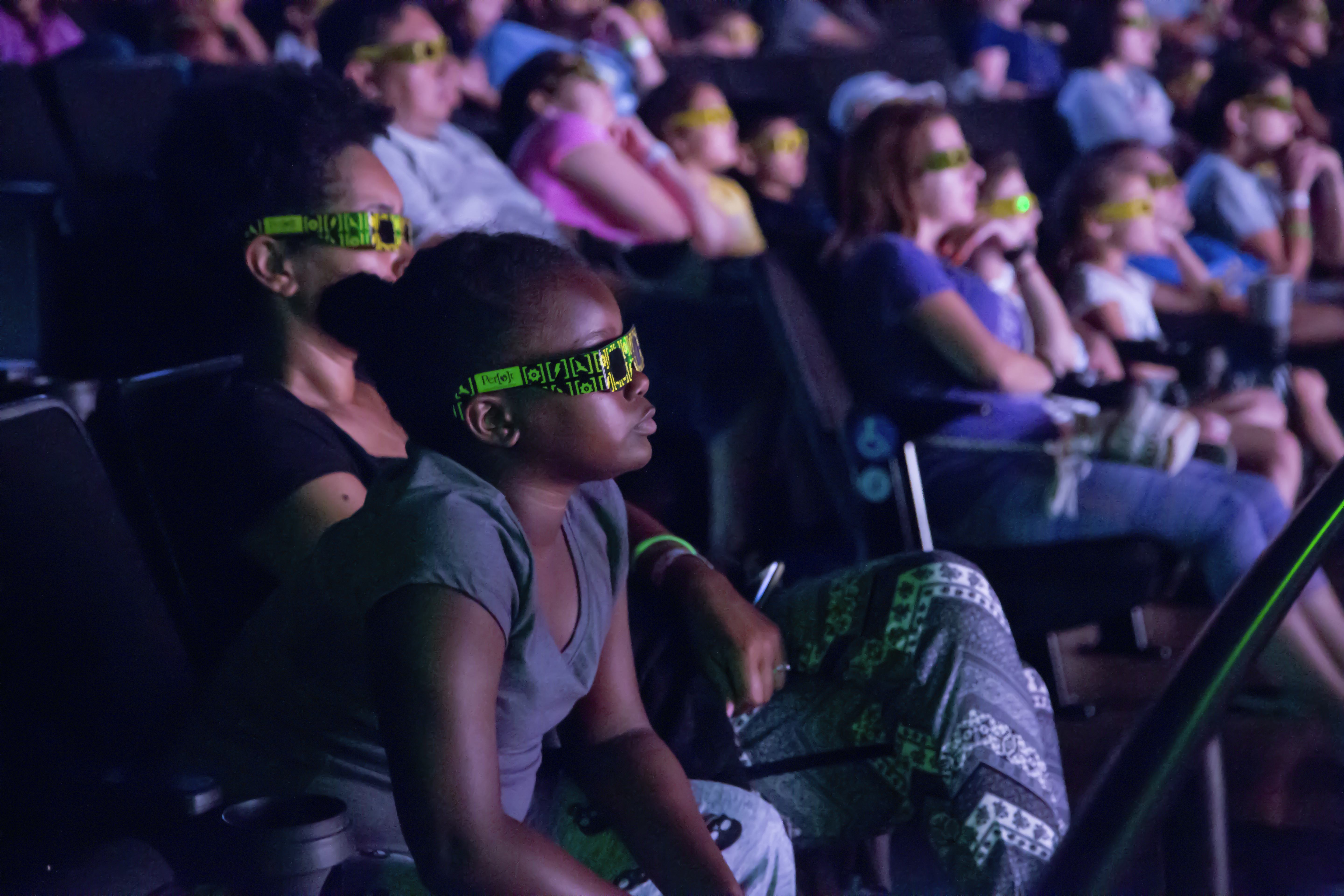 A young girl watching a movie in the Perot Museum theater with 3D glasses on.