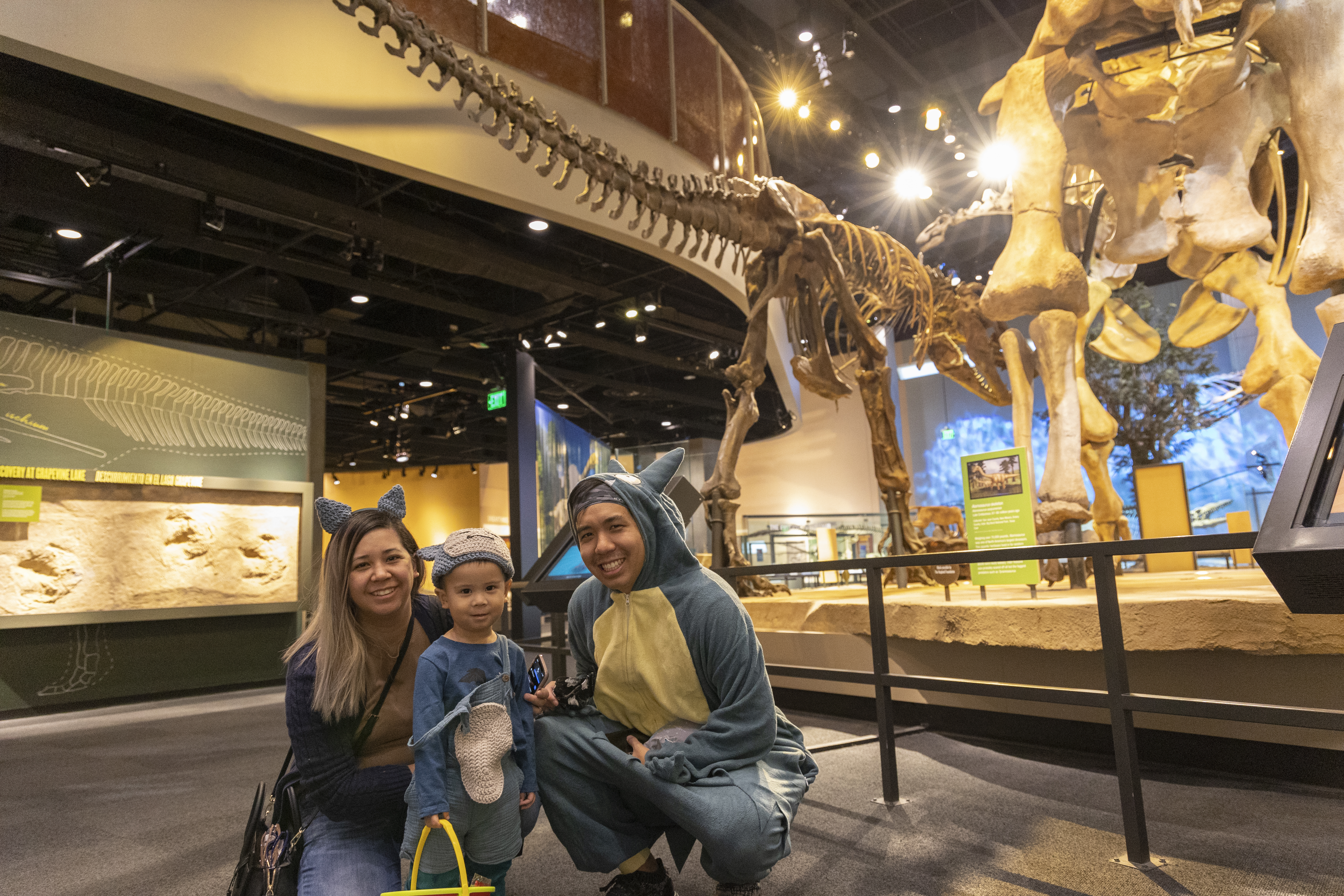 Family dressed in dinosaur costumes posing in front of large dinosaur fossil