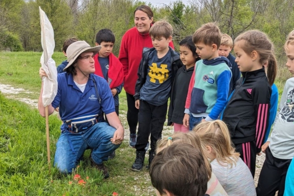 Adult man kneeling in grass in front on standing children looking at flowers